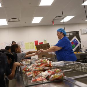 A food service employee hands out lunch to students