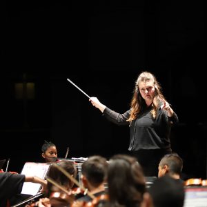 A middle school teacher conducts her orchestra