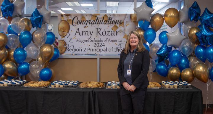 West Career and Technical Academy Principal Amy Dockter-Rozar poses in front of an arrangement of treats, balloons and a sign celebrating her Regional Principal of the Year win by Magnet Schools of America.