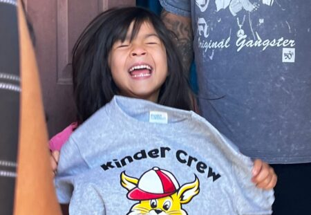 Future Kindergartener laughs and shows great joy with her new Kinder Crew tshirt.